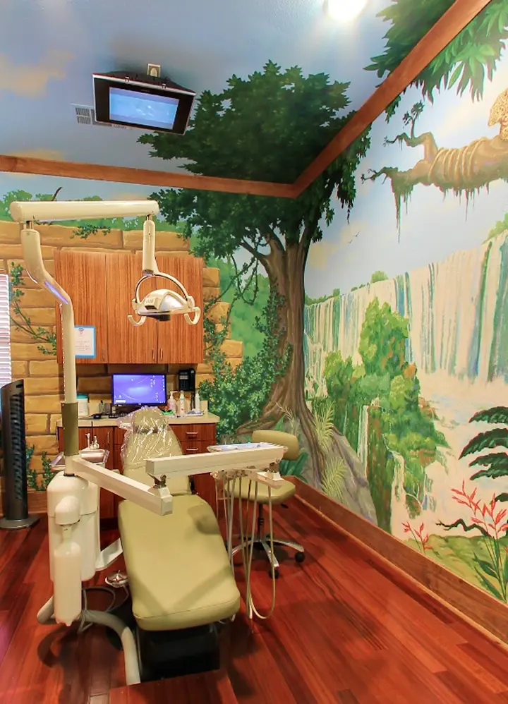Child-friendly dental operatory with jungle mural, green patient chair, and overhead monitor at McKinney pediatric dental pr.