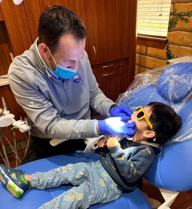 Pediatric dentist examining young patient's teeth during dental cleaning and exam visit.