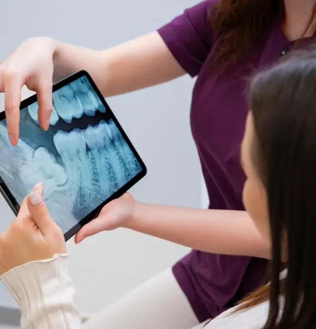Dentist and patient reviewing digital dental X-rays on tablet together.