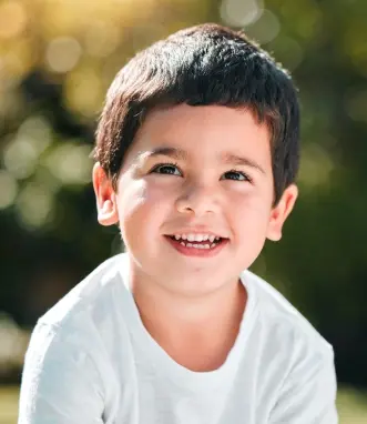 Happy young boy smiling outdoors in white shirt for dental practice emergency care page.