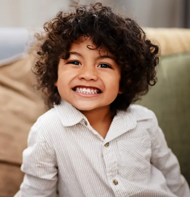 Young child with curly dark hair smiling brightly after fluoride treatment.
