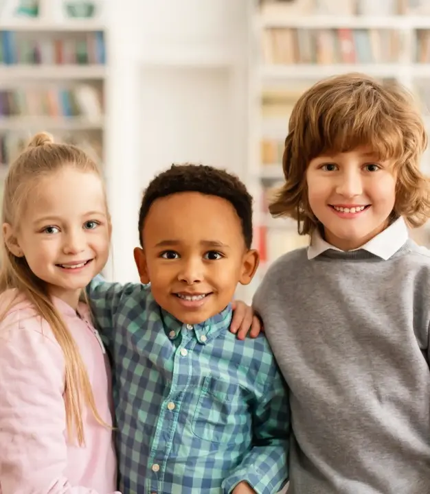 Three smiling children in a bright dental office with bookshelves in McKinney.