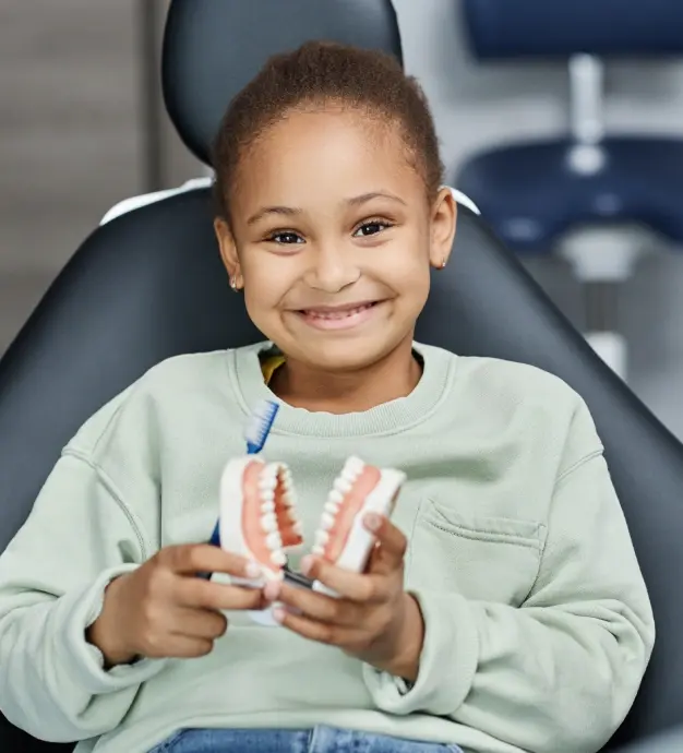 Young patient smiling while holding a dental teeth model in a McKinney dental office.