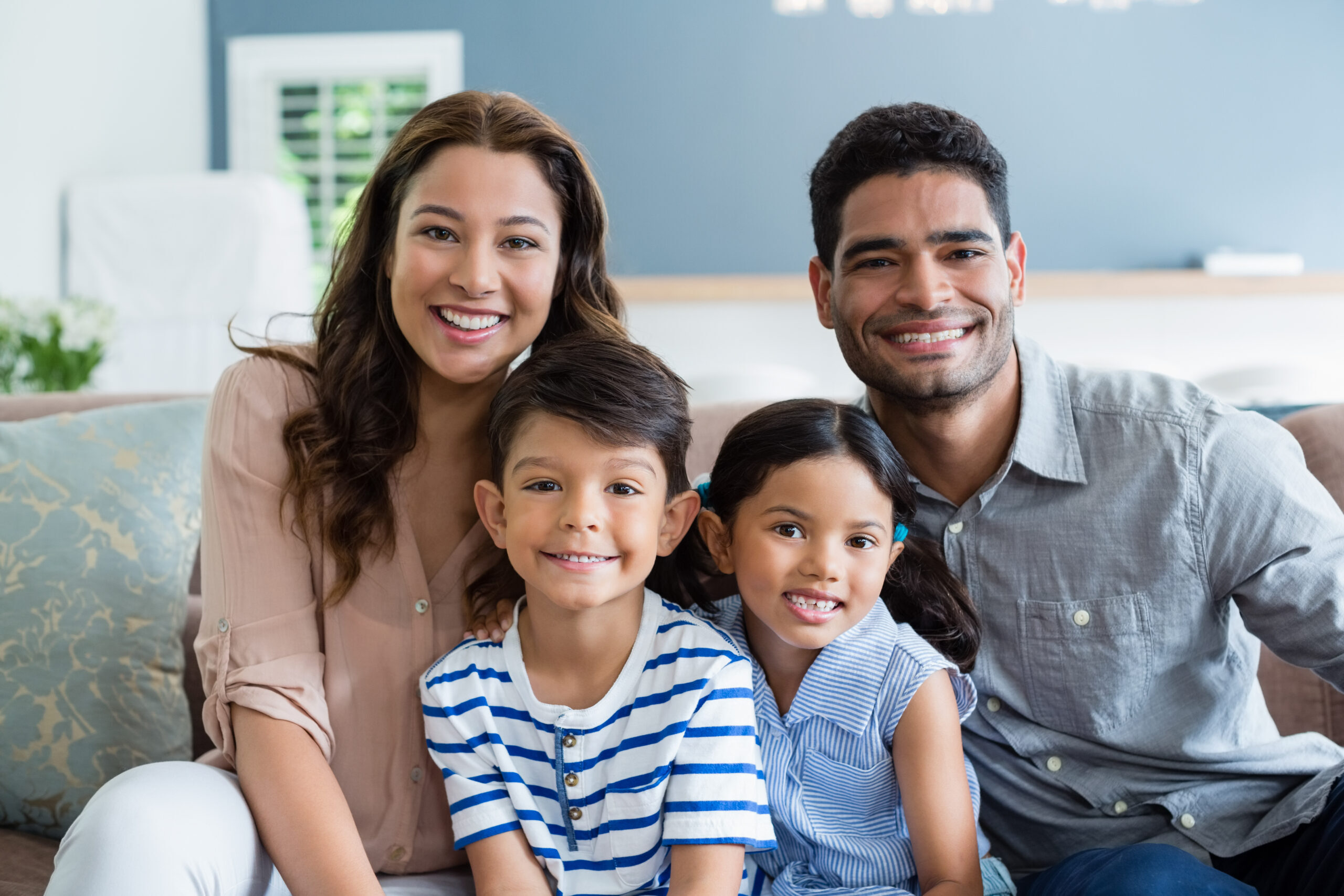Happy family of four smiling together on a couch in a dental office setting.